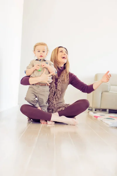 Feliz madre sentada en el suelo con su bebé y sonriendo . —  Fotos de Stock