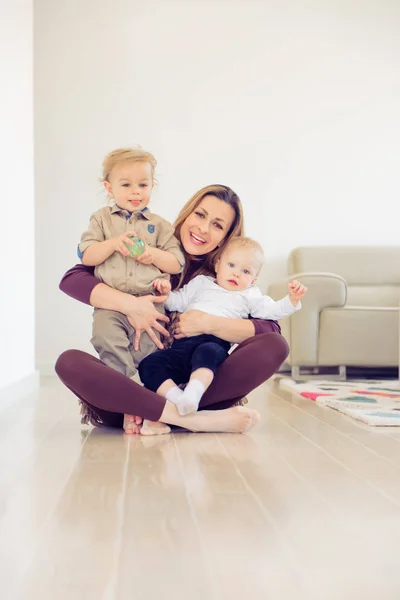 Feliz madre sentada en el suelo con sus dos bebés y jugando —  Fotos de Stock