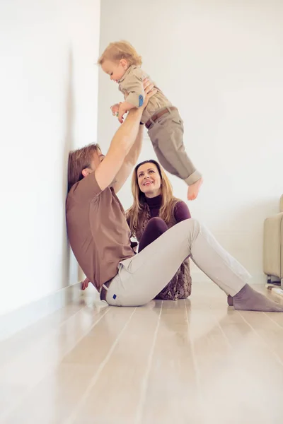 Famiglia felice seduta sul pavimento con il loro bambino piccolo. Famiglia trascorrere del tempo a casa con il figlio. Padre crescere suo figlio in aria . — Foto Stock