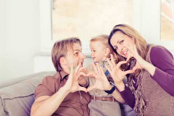 Ritratto di famiglia felice seduta sul divano e sorridente. Amore a forma di cuore . — Foto Stock