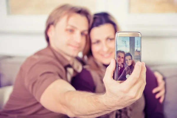Felice giovane coppia seduta sul divano e fare selfie — Foto Stock