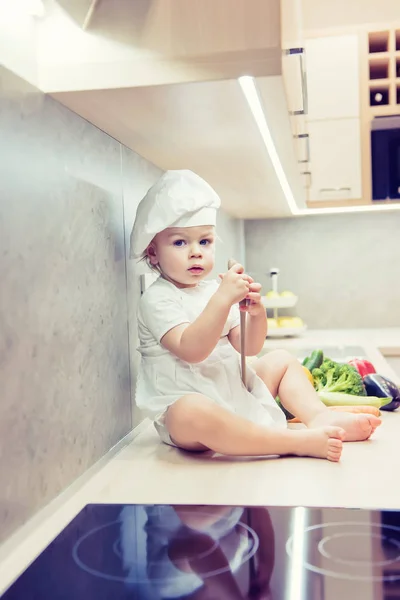 Menino sentado entre vegetais na cozinha e se prepara para cozinhar — Fotografia de Stock