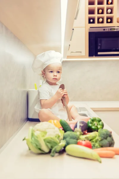 Menino sentado entre vegetais na cozinha e se prepara para cozinhar — Fotografia de Stock