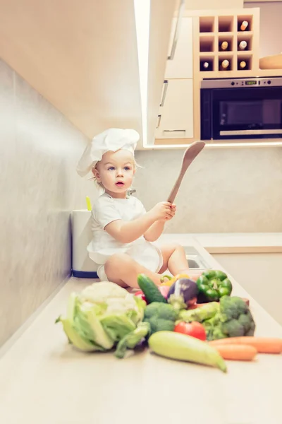 Menino sentado entre vegetais na cozinha e se prepara para cozinhar — Fotografia de Stock