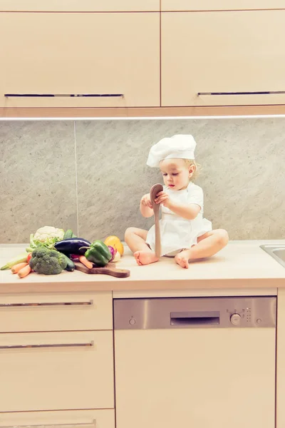 Menino sentado entre vegetais na cozinha e se prepara para cozinhar — Fotografia de Stock