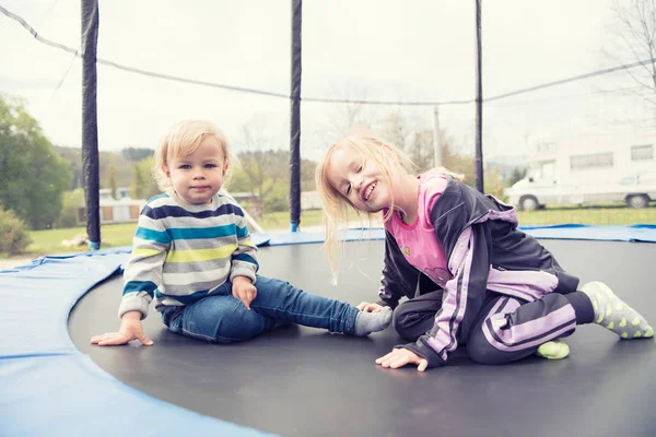 Dwa piękne dzieci siedzi na trampolinie i pozowanie. Czas odpoczynku i przygotowanie do skoków. — Zdjęcie stockowe