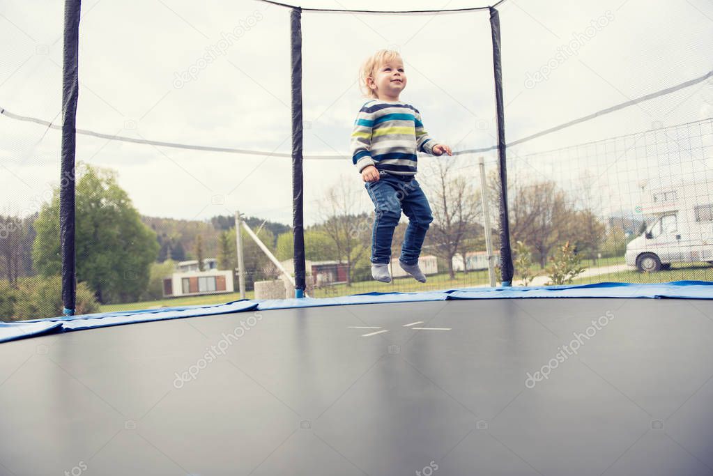 Beautiful little boy jumping on the trampoline outdoor.