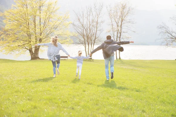 Buon padre, madre e bambina che corrono lungo il lago e godono in una bella giornata di sole . — Foto Stock