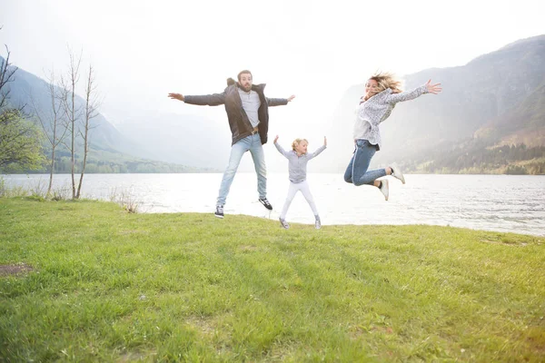 Счастливый отец, мать и маленькая девочка прыгают возле озера в прекрасный солнечный день . — стоковое фото