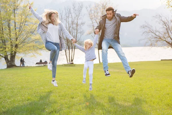 Щасливий батько, мати і маленька дівчинка стрибають біля озера в красивий сонячний день . — стокове фото