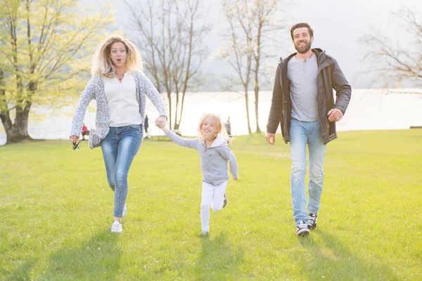 Щасливий батько, мати і маленька дівчинка бігають біля озера і насолоджуються прекрасним сонячним днем . — стокове фото