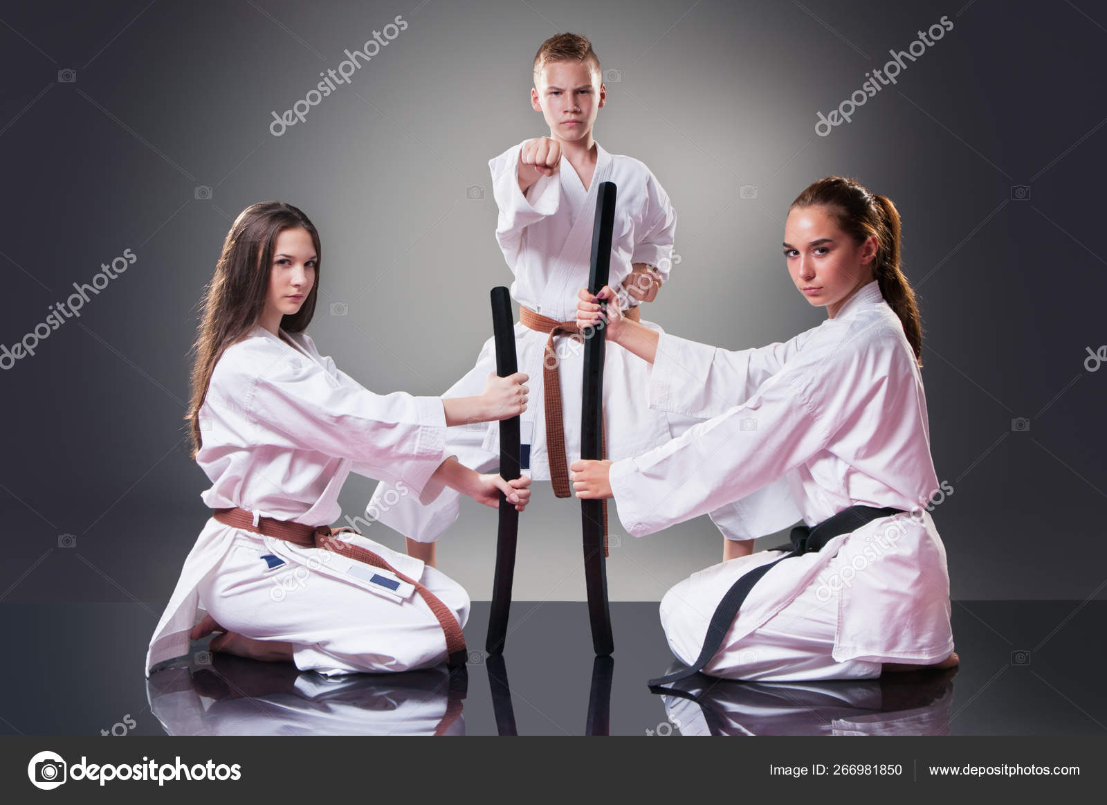 Beautiful young female karate players posing with sword on the gray background. Male fighter in