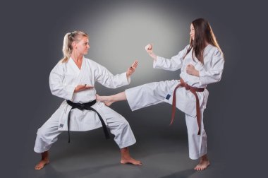 Güzel genç kadın karate oyuncusu gri arka plan üzerinde tekme yapıyor