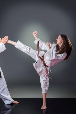Güzel genç kadın karate oyuncusu gri arka plan üzerinde tekme yapıyor