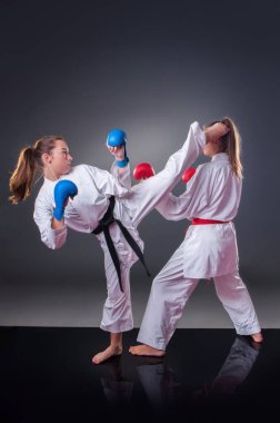 Güzel genç kadın karate oyuncusu gri arka plan üzerinde tekme yapıyor