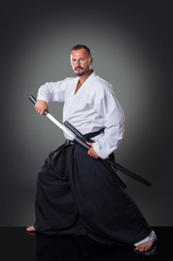 Yakışıklı erkek karateoyuncusu gri arka plan üzerinde kılıç ile poz.