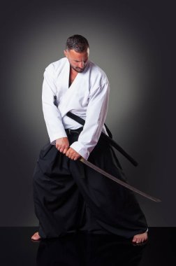 Yakışıklı erkek karateoyuncusu gri arka plan üzerinde kılıç ile poz.