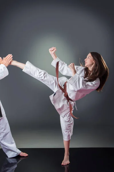 Krásná mladá ženská karate hráčka, co kopne do šedého pozadí — Stock fotografie