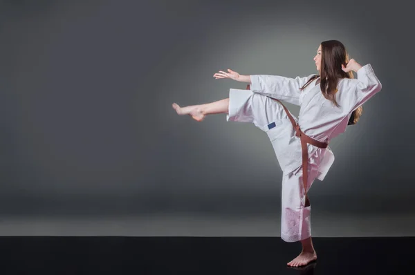 Krásná mladá ženská karate hráčka, co kopne do šedého pozadí — Stock fotografie