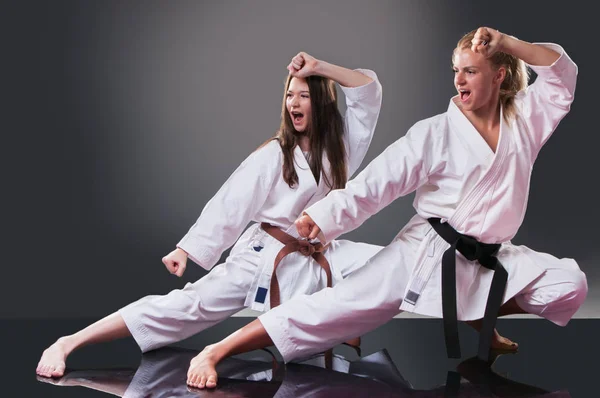 Dvě nádherné mladé ženské karate hráči na Kata na šedém pozadí — Stock fotografie