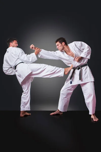 Schöner junger männlicher Karatespieler beim Kicken vor grauem Hintergrund — Stockfoto