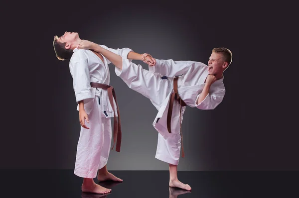 Knappe jonge mannelijke Karate speler doen kick op de grijze achtergrond — Stockfoto