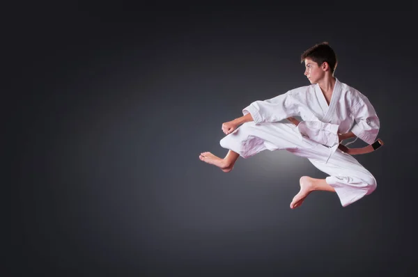 Guapo joven jugador de karate masculino haciendo patada en el fondo gris —  Fotos de Stock