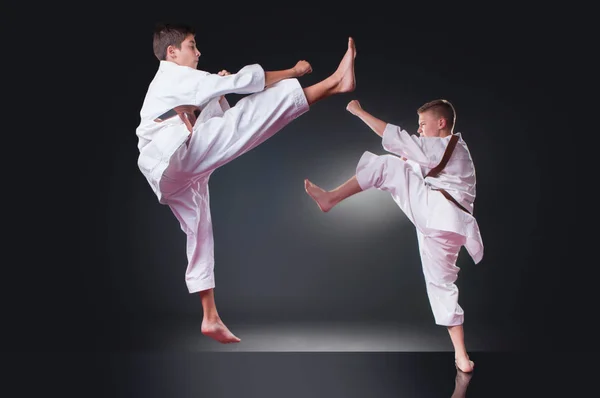 Bello giovani giocatori di karate maschile che fanno calci sullo sfondo grigio — Foto Stock