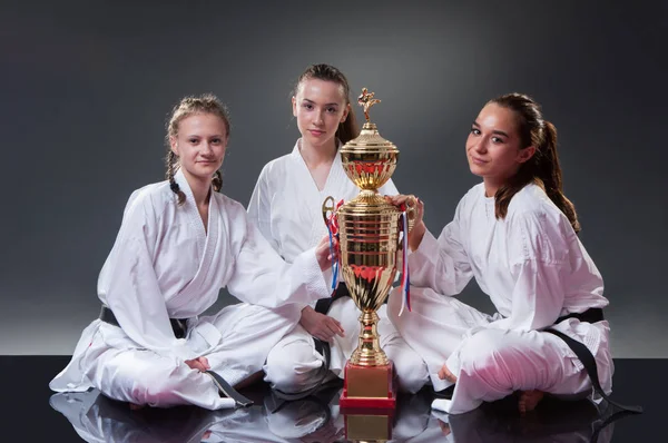 Grupa pięknych kobiet Karate graczy stwarzających z filiżanką na szarym tle. Obchodzi 1 miejsce. — Zdjęcie stockowe