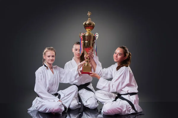 Group of beautiful female karate players posing with the cup on the gray background. Celebrating 1st place.