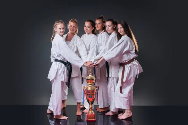 Groupe de belles joueuses de karaté posant avec la tasse sur le fond gris. Célébrer la 1ère place . — Photo