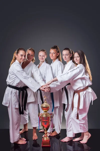 Groupe de belles joueuses de karaté posant avec la tasse sur le fond gris. Célébrer la 1ère place . — Photo