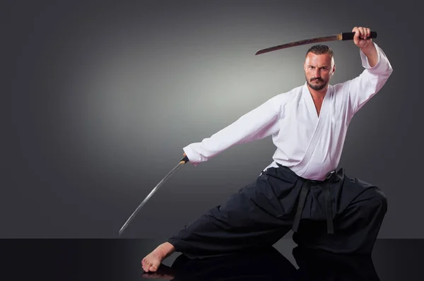 Handsome male karate player posing with the sword on the gray background.