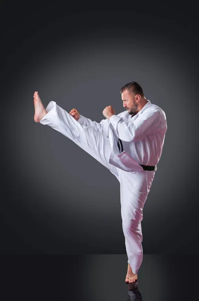 Przystojny mężczyzna Karate gracz robi kick na szarym tle — Zdjęcie stockowe