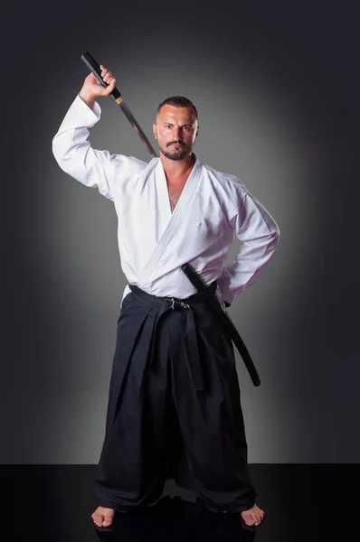 Krásný mužský hráč karate pózný s mečem na šedém pozadí. — Stock fotografie