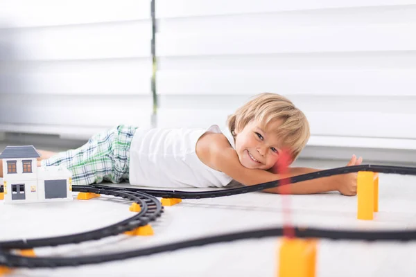 Lindo niño chico tendido en el suelo y jugando con juguete railw — Foto de Stock