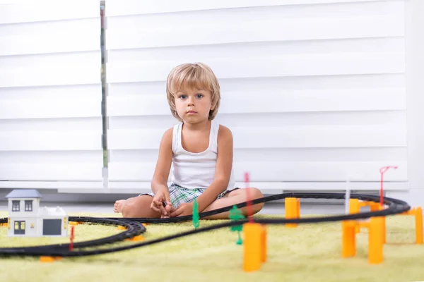 Lindo niño jugando con juguete ferrocarril carretera en casa en el suelo — Foto de Stock