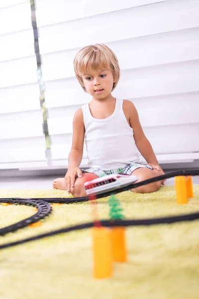 Lindo niño jugando con juguete ferrocarril carretera en casa en el suelo — Foto de Stock