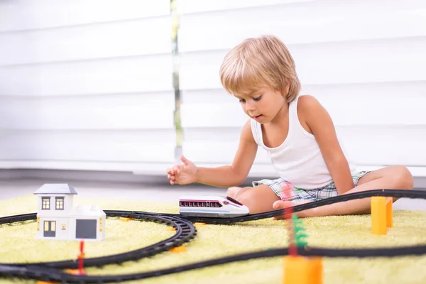 Lindo niño jugando con juguete ferrocarril carretera en casa en el suelo — Foto de Stock