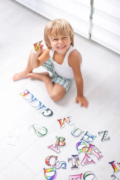 漂亮的小男孩在家里的地板上学习字母. 图库图片
