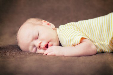 Yeni doğmuş güzel erkek bebek yumuşak kahverengi battaniyenin üzerinde huzur içinde uyuyor.