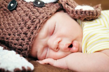 Şirin şapkalı yeni doğmuş güzel erkek bebek yumuşak kahverengi battaniyenin üzerinde huzur içinde uyuyor.