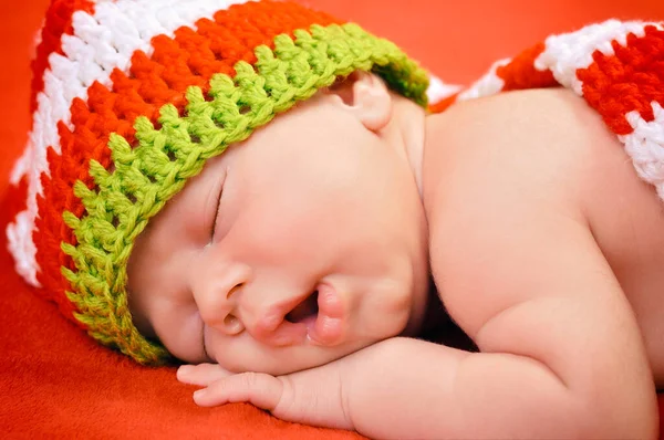 可愛い帽子をかぶった美しい新生児の男の子が柔らかい赤い毛布の上に静かに眠る — ストック写真
