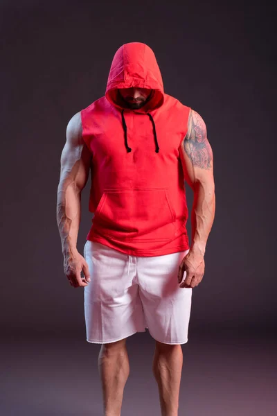 フード付きの強力な筋肉質の男が赤いスウェットシャツを着てポーズをとっている スタジオ撮影で赤と青の煙 — ストック写真