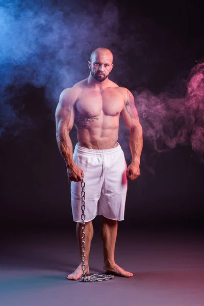 强壮健壮的男人赤身裸体地戴着链子摆姿势 带着红色和蓝色烟雾的工作室拍摄 — 图库照片