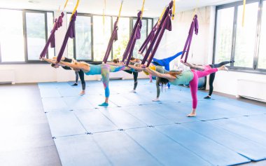 Bir grup genç kadın ve yerçekimsiz yoga egzersizleri yapan kaslı bir adam. Fly fitness. Mor hamak