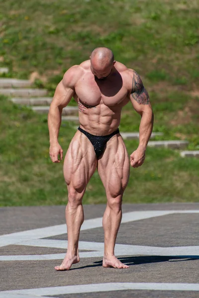 Powerful muscular bodybuilder in panties posing at the park. Quadriceps and upper body contraction