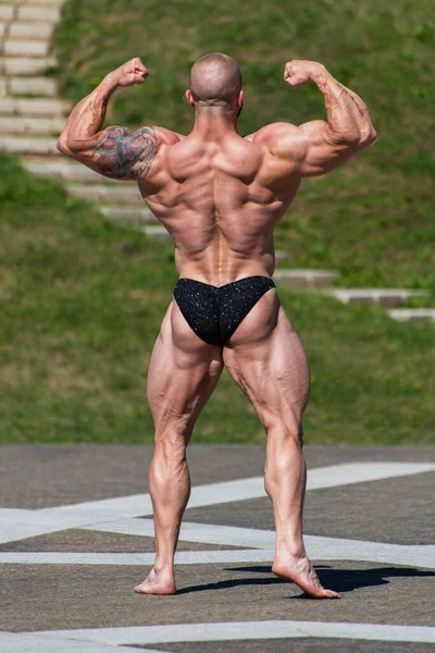 身穿内裤的强壮强壮的健美健美运动员摆出一副公园的姿势 四头肌和上半身收缩 — 图库照片