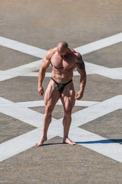 身穿内裤的强壮强壮的健美健美运动员摆出一副公园的姿势 四头肌收缩 图库图片