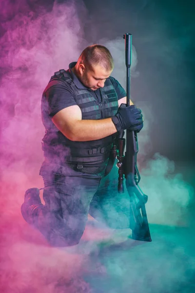 士兵从战场上的烟雾中走出来 军事特别行动的概念 用霰弹枪跪着摆姿势 免版税图库图片